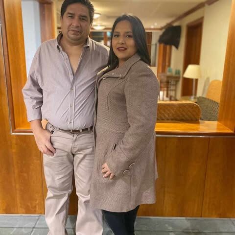 Efren and Lilian pose for the camera. They have dark hair and are dressed smartly in a shirt and smart coat.