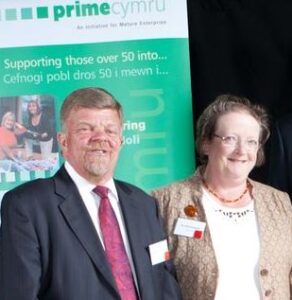 Hugh and Ann smile with a PRIME Cymru banner in the background