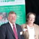 Hugh and Ann smile with a PRIME Cymru banner in the background