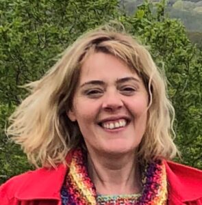Nerys is a smiling woman wearing a bright red coat and has shoulder length blonde hair