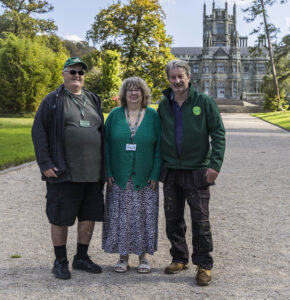 David smiles at the camera with Volunteer Mentor, Nick Carruthers to the right and Tracy Robbins, Friends of Margam Park Officer in the centre. In the background is Margam Park Castle. It is a bright, sunny day.